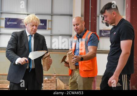 Premierminister Boris Johnson (links) baut bei einem Besuch des Exeter College mit einer Kelle eine Ziegelmauer. Der Besuch kommt vor einer Rede, in der er voraussichtlich garantierte Möglichkeiten für lebenslanges Lernen ankündigen wird, um zur Schaffung von Arbeitsplätzen nach der Pandemie beizutragen. Stockfoto