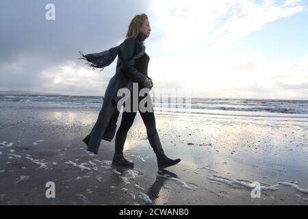 Eine Frau aus weißem Kaukasus mittleren Alters am Strand von Troon, Ayrshire, mit einem herannahenden Sturm, der auf die Wetterfront blickt, und einem melandionisch-nachdenklichen Spaziergang am Strand. Ein Konzeptbild für ein Cover oder melacholy, Einsamkeit. Verlorene Liebe Stockfoto