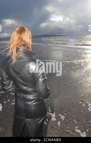 Eine Frau aus weißem Kaukasus mittleren Alters am Strand von Troon, Ayrshire, mit einem herannahenden Sturm, der auf die Wetterfront blickt, und einem melandionisch-nachdenklichen Spaziergang am Strand. Ein Konzeptbild für ein Cover oder melacholy, Einsamkeit. Verlorene Liebe Stockfoto