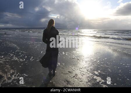 Eine Frau aus weißem Kaukasus mittleren Alters am Strand von Troon, Ayrshire, mit einem herannahenden Sturm, der auf die Wetterfront blickt, und einem melandionisch-nachdenklichen Spaziergang am Strand. Ein Konzeptbild für ein Cover oder melacholy, Einsamkeit. Verlorene Liebe Stockfoto