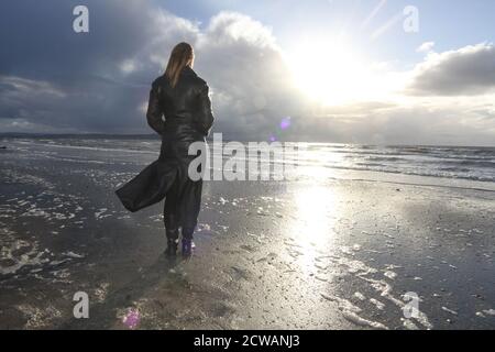 Eine Frau aus weißem Kaukasus mittleren Alters am Strand von Troon, Ayrshire, mit einem herannahenden Sturm, der auf die Wetterfront blickt, und einem melandionisch-nachdenklichen Spaziergang am Strand. Ein Konzeptbild für ein Cover oder melacholy, Einsamkeit. Verlorene Liebe Stockfoto