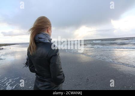 Eine Frau aus weißem Kaukasus mittleren Alters am Strand von Troon, Ayrshire, mit einem herannahenden Sturm, der auf die Wetterfront blickt, und einem melandionisch-nachdenklichen Spaziergang am Strand. Ein Konzeptbild für ein Cover oder melacholy, Einsamkeit. Verlorene Liebe Stockfoto