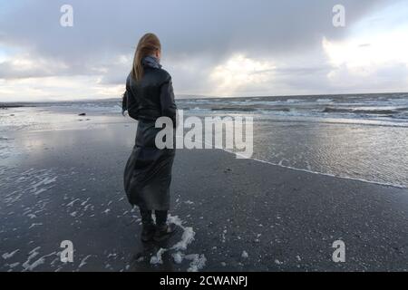 Eine Frau aus weißem Kaukasus mittleren Alters am Strand von Troon, Ayrshire, mit einem herannahenden Sturm, der auf die Wetterfront blickt, und einem melandionisch-nachdenklichen Spaziergang am Strand. Ein Konzeptbild für ein Cover oder melacholy, Einsamkeit. Verlorene Liebe Stockfoto