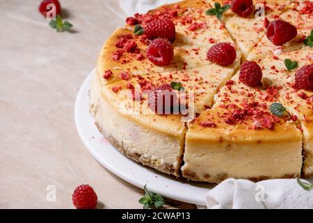 Hausgemachte Himbeer gebackenen Käsekuchen auf Teller geschnitten, dekoriert mit frischen Himbeeren und Minze auf rosa Marmor Hintergrund mit weißem Tuch. Nahaufnahme Stockfoto