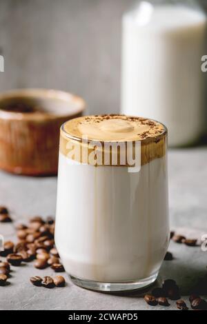Dalgona schaumig Kaffee Trend koreanisch trinken Milch Latte mit Kaffee-Schaum in Glas Becher, dekoriert mit gemahlenem Kaffee auf grauen Textur Tisch. Zutaten oben Stockfoto