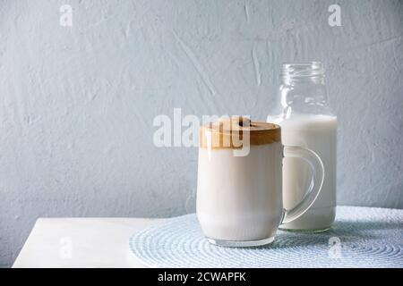Dalgona schaumig Kaffee Trend koreanisch trinken Milch Latte mit Kaffee-Schaum in Glas Becher, Flasche Milch auf weißem Marmor Tisch. Kopierbereich Stockfoto