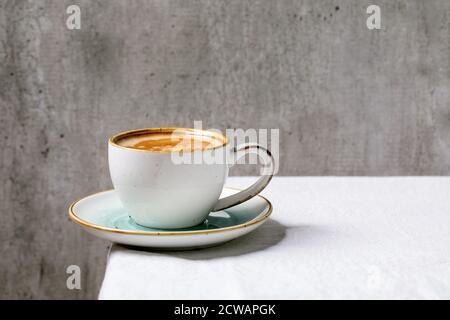 Schwarzer Kaffee Espresso mit Schaum in weißer Keramik-Tasse mit Untertasse auf weißem Baumwolltischtuch stehend. Kopierbereich Stockfoto