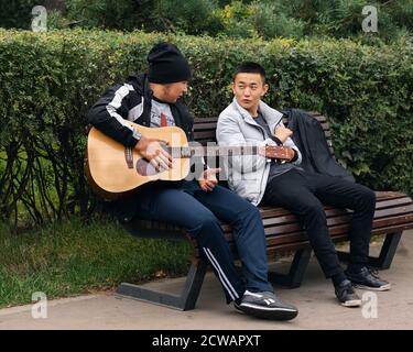 Moskau/Russland - Sep 2020: Zwei junge Männer spielen Gitarre auf einer Parkbank. Stockfoto