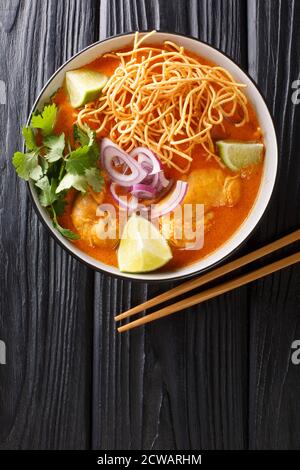 Khao Soi ist eine beliebte Kokos-Curry-Nudelsuppe mit Hühnerfleisch in der Schüssel auf dem Tisch. Vertikale Draufsicht von oben Stockfoto