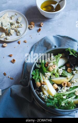 Herbstsalat in einer dunkelgrauen Schüssel. Gemischte Blätter mit Birnenscheiben, Blauschimmelkäse, gerösteten Haselnüssen und einem Honigdressing. Stockfoto