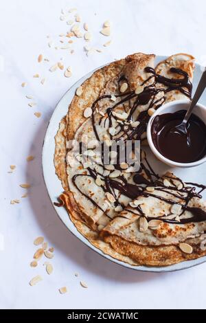 Stapel von gefalteten Crepes auf einem großen Teller mit einem Nieselregen von dunkler Schokoladensauce und gerösteten Mandeln. Stockfoto