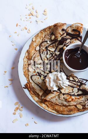 Stapel von französischen Crepes auf einem großen Teller mit einem Nieselregen von dunkler Schokoladensauce, gerösteten Mandeln und einem Puppe Schlagsahne. Stockfoto