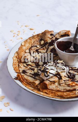 Stapel von französischen Crepes auf einem großen Teller mit einem Nieselregen von dunkler Schokoladensauce, gerösteten Mandeln und einem Puppe Schlagsahne. Stockfoto