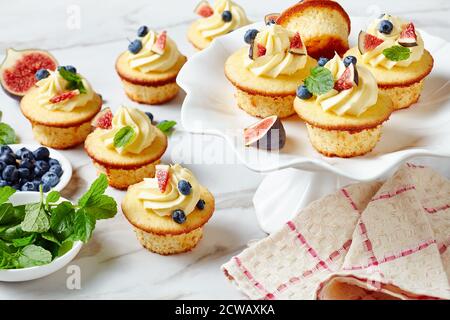 Köstliche Cupcakes mit Vanillecreme verziert mit frischen Feigen und Heidelbeeren auf einem Kuchenständer auf einem Marmortisch, Landschaftsansicht von oben, Stockfoto