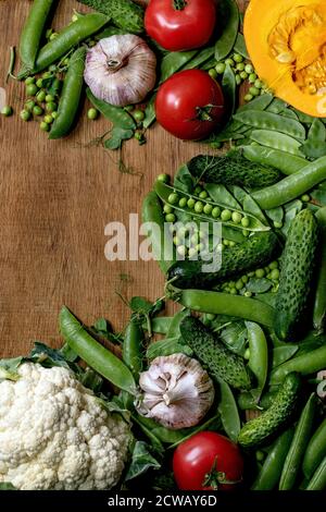 Vielfalt an frischem rohem Bio-Gemüse zum Kochen. Die Hälfte des hokkaido Kürbis, junge grüne Erbse, Blumenkohl, Knoblauch, Gurken, Tomaten über Holz Stockfoto