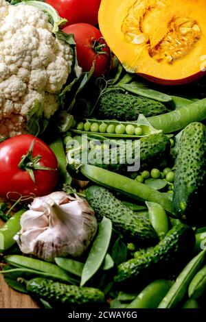 Vielfalt an frischem rohem Bio-Gemüse zum Kochen. Die Hälfte des hokkaido Kürbis, junge grüne Erbse, Blumenkohl, Knoblauch, Gurken, Tomaten über Holz Stockfoto