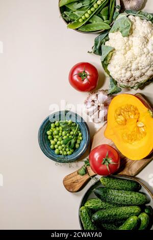 Vielfalt an frischem rohem Bio-Gemüse zum Kochen. Die Hälfte des hokkaido Kürbis, junge grüne Erbse, Blumenkohl, Knoblauch, Gurken, Tomaten über beige b Stockfoto