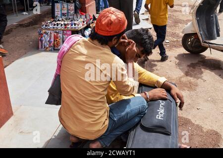 Ein Mann reinigt Kundenohr, Ohrenschmalz für Geld auf vielbefahrenen Straße in chandani chowk, alt delhi, indien. Stockfoto