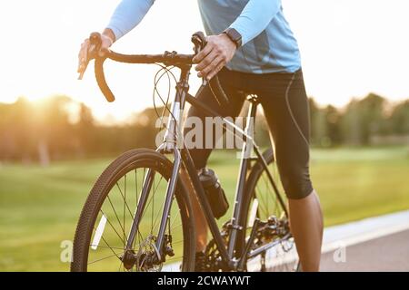 Kurzer Schuss von professionellen Rennrad-Rennfahrer in Sportbekleidung Radfahren im Freien bei Sonnenuntergang, Mann mit Fahrrad auf der Straße im Freien stehen. Aktiver Lebensstil und Sport Stockfoto