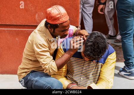 Ein Mann reinigt Kundenohr, Ohrenschmalz für Geld auf vielbefahrenen Straße in chandani chowk, alt delhi, indien. Stockfoto