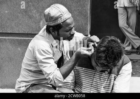 Ein Mann reinigt Kundenohr, Ohrenschmalz für Geld auf vielbefahrenen Straße in chandani chowk, alt delhi, indien. Stockfoto