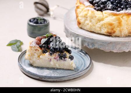 Hausgemachte Heidelbeere gebacken weichen Käsekuchen san sebastian, ganz und in Scheiben geschnitten, auf Keramik-Kuchen Stand Teller mit frischen Waldbeeren, Puderzucker und dekoriert Stockfoto