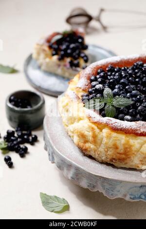 Hausgemachte Heidelbeere gebacken weichen Käsekuchen san sebastian, ganz und in Scheiben geschnitten, auf Keramik-Kuchen Stand Teller mit frischen Waldbeeren, Puderzucker und dekoriert Stockfoto