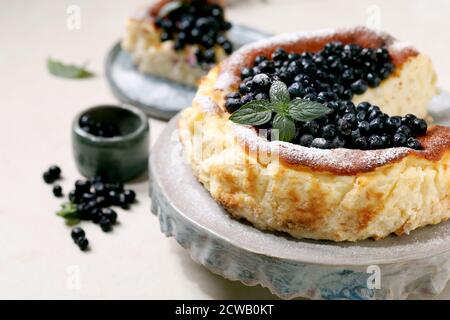 Hausgemachte Heidelbeere gebacken weichen Käsekuchen san sebastian, ganz und in Scheiben geschnitten, auf Keramik-Kuchen Stand Teller mit frischen Waldbeeren, Puderzucker und dekoriert Stockfoto