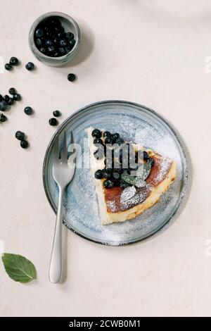 Stück hausgemachten Heidelbeere gebacken weichen Käsekuchen san sebastian auf Keramik-Teller, dekoriert von frischen Waldbeeren, Puderzucker und Minze über weißen tex Stockfoto