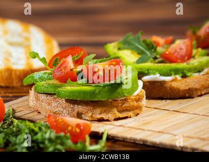 Avocado-Maische und frisch geschnittene Tomaten auf gegrilltem Toastbrot auf braunem Holzhintergrund. Trendiges und gesundes Frühstück. Stockfoto
