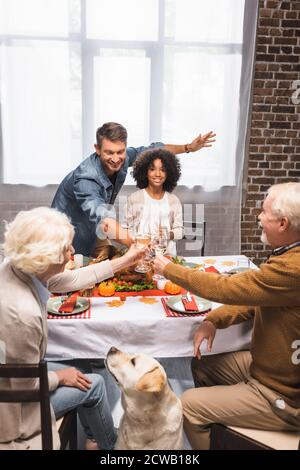 Selektiver Fokus von Golden Retriever in der Nähe von multikulturellen Familie Klickgläser Von Weißwein weiß feiern Danksagung Stockfoto