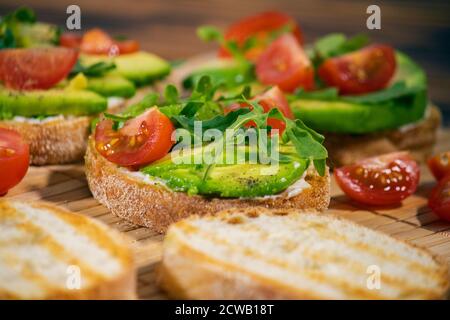 Avocado-Maische und frisch geschnittene Tomaten auf gegrilltem Toastbrot auf braunem Holzhintergrund. Trendiges und gesundes Frühstück. Stockfoto