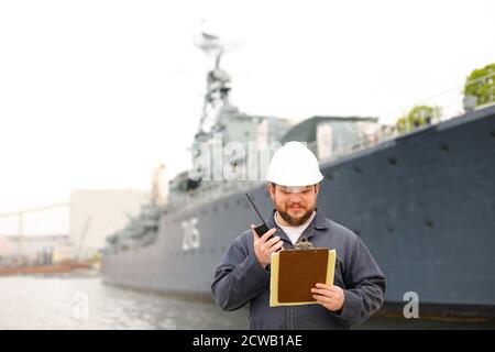 Marine Assistant Engineer im Gespräch mit Walkie Talkie Radio und in der Nähe des Schiffes mit Dokumenten in den Händen stehen. Stockfoto