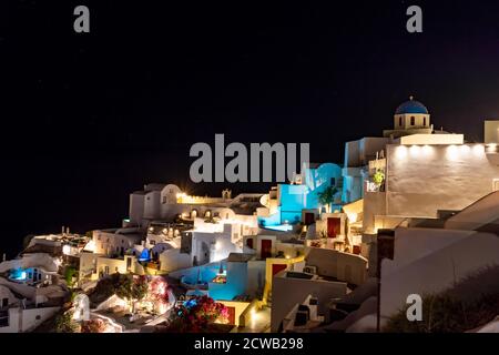 Die Nacht fällt auf das griechische Dorf Oia auf der Insel Santorini. Typische orthodoxe Kirche mit runden und blauen Dach überhängt die Stadt Stockfoto