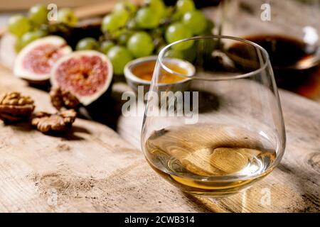 Gläser von Rot- und Weißwein mit Trauben, Feigen, Ziegenkäse und Walnüssen auf altem Holzhintergrund. Nahaufnahme Stockfoto