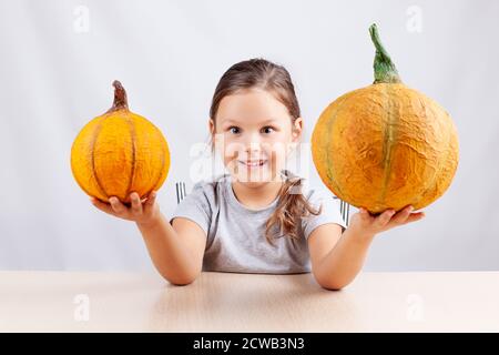 Ein glückliches Kind auf weißem Hintergrund hält selbstgemachte Pappmaché Kürbisse für Halloween Stockfoto