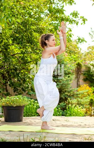 Junge Frau praktiziert Yoga im Sommergarten - Garudasana oder Adler Pose. Stockfoto