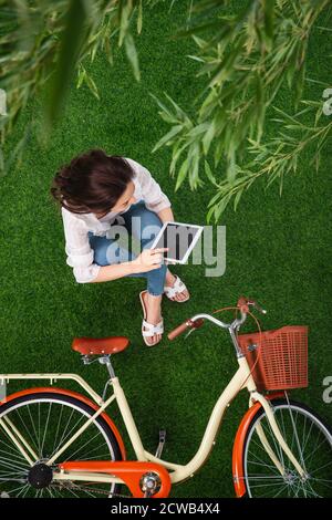 Junge Frau sitzt auf dem Gras, um Tablet zu verwenden Stockfoto