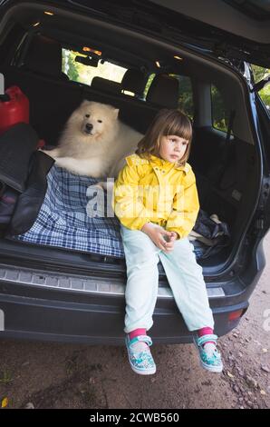 Kleines Mädchen und Samoyed Hund sitzt in einem Kofferraum von suv-Familienauto, vertikale Foto Stockfoto