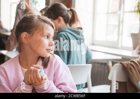 Blonde kaukasische kleine Mädchen mit einem Spielzeug in rosa Kapuzenpullover sitzt in einer Cafeteria, close-up-Profil Porträt Stockfoto
