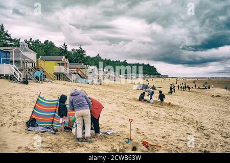 Landschaftlich reizvolle Landschaft des breiten Strandsandes bei Holkham im Norden Norfolks, England mit Strandhütten und Familien unter stürmischem Himmel Stockfoto
