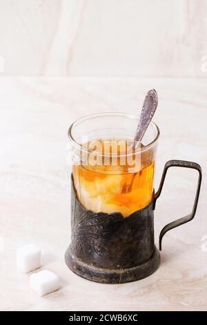 Milch löst sich in Retro-Tasse heißen Tee in Vintage Glashalter mit Tee-Löffel und Zucker Würfel über weißen Marmor Backgtound. Stockfoto