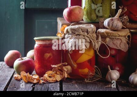 Sammlung Set von vielen hausgemachten Gläsern mit Konserven (Gurken, Tomaten, Paprika), mit Knoblauch und frischen und getrockneten Äpfeln. Über altem Holz Stockfoto