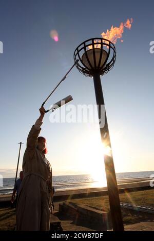 Prestwick, Ayrshire, Schottland Großbritannien 05. Juni 2012 Beleuchtung eines Leuchtfeuers am Prestwick Beach zur Feier der Olympischen Spiele 2012 mit der Isle of Arran und dem Firth of Clyde Ground ging die Sonne unter, so dass es einen Lichtreflexe vom sunlight.beacons. Oder Feuerfeuer, waren Feuer, die angezündet wurden, um die lokalen Menschen vor dem Herannahen eines Feindes zu warnen. Sie lagen auf hohen Hügeln, in der Regel als Teil eines defensiven Signalsystems oder einer Kette, die sich von der Küste bis ins Landesinnere erstreckte. Das Signal wurde durch Rauch am Tag und Licht in der Nacht gegeben. Stockfoto