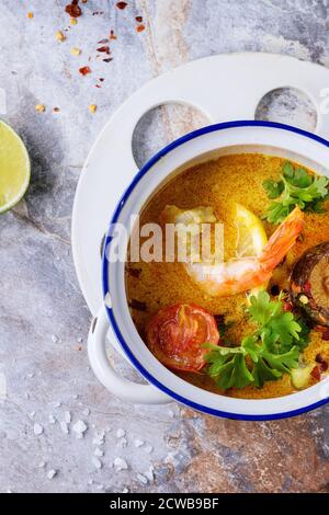 Weiße Keramikpfanne mit würziger Thai-Suppe Tom Yam mit Kokosmilch, Chili und Meeresfrüchten auf grauem Steingrund. Draufsicht Stockfoto