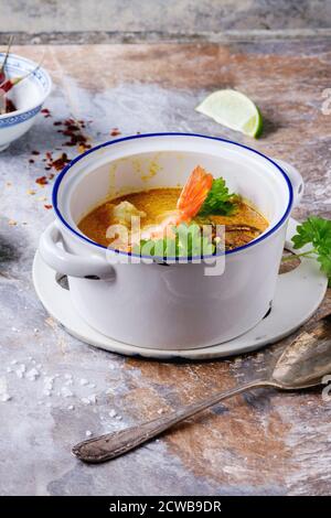 Weiße Keramikpfanne mit würziger Thai-Suppe Tom Yam mit Kokosmilch, Chili und Meeresfrüchten auf grauem Steingrund. Stockfoto