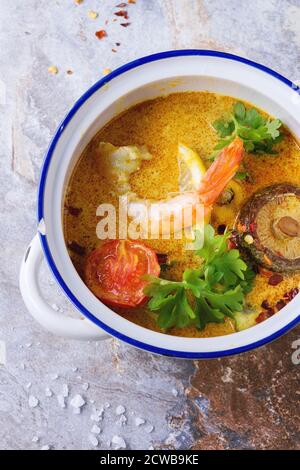 Weiße Keramik Pfanne mit würzigen Thai Suppe Tom Yam mit Kokosmilch, Chili-Pfeffer und Garnelen auf grauem Stein Hintergrund. Ansicht von oben Stockfoto