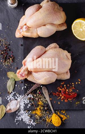 Zwei Raw Mini Chicken mit Meersalz und verschiedenen Gewürzen auf schwarzem Schieferbrett. Draufsicht Stockfoto