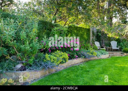 Landschaftlich schöner, sonniger privater Garten (modernes Design, farbenfrohe Sommerblumen, Randpflanzen, Sitzmöbel auf der Terrasse, Rasen) - Yorkshire, England, Großbritannien Stockfoto