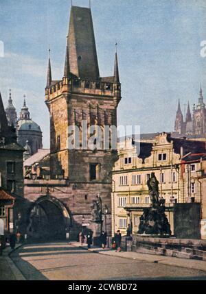 Die Altstadt Ende der König-Charles-Brücke, Prag, Tschechische Republik, 1943. Der Bau der Brücke über die Moldau begann 1357 unter der Herrschaft von Karl IV., König von Böhmen und Kaiser des Heiligen Römischen Reiches. Die Brücke ist aus Stein gebaut, 516 Meter lang, und hat 16 Bögen mit Eiswächtern geschützt. Die Brücke wird von zwei Reihen von 15 Statuen flankiert. Ein Druck aus Signal, Februar 1943. Signal war eine Zeitschrift des Deutschen Dritten Reiches von 1940 bis 1945. Der Künstler ist unbekannt. Stockfoto